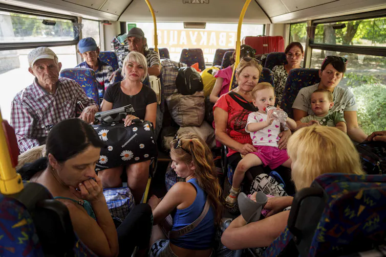 Un groupe de personnes, adultes en enfants, sont debout ou assis dans un autobus bondé