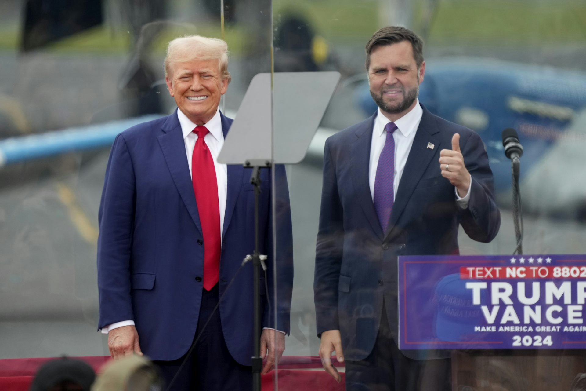 Donald Trump et JD Vance, pouce en l’air, devant devant un micro