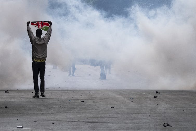 A protester stands holding the Kenyan flag in front a plume of smoke.