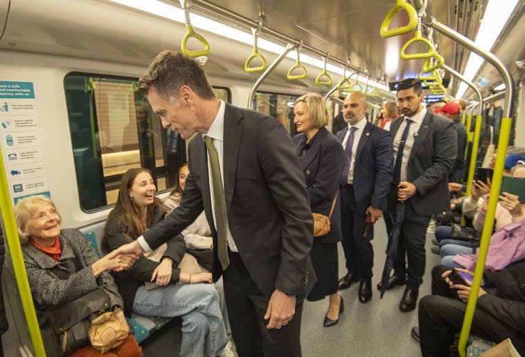A man in a suit shakes hands with an seated passenger on a train