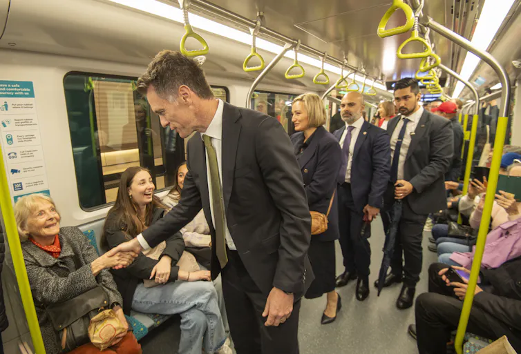 A man in a suit shakes hands with an seated passenger on a train