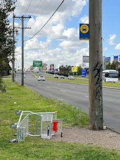 A bus top sign on a power pole with a shopping trolley abandoned next to it