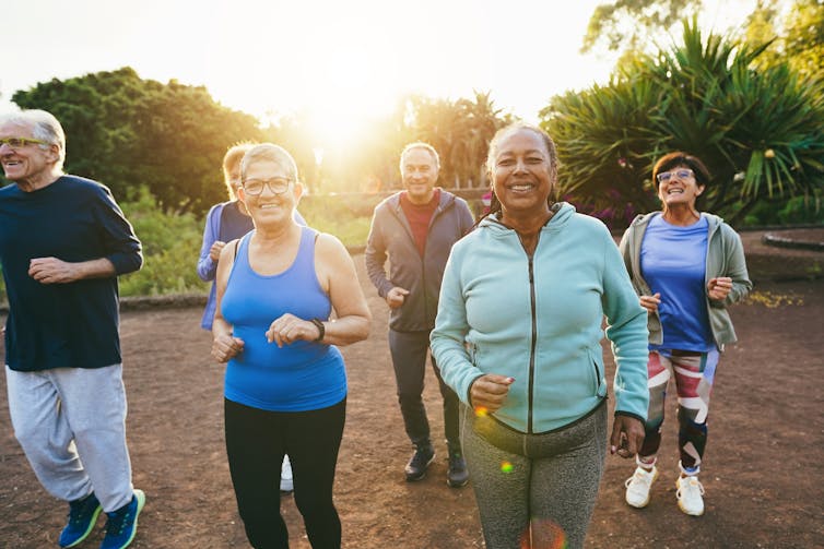 A group of older adults exercising outdoors, all smiling.