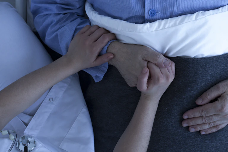From above, a female nurse's hands holding hands of a man lying inbed.