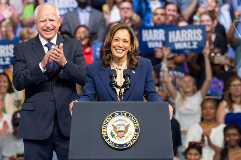 Kamala Harris at a podium with Tim Walz behind her.