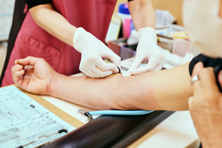 A nurse drawing blood from a senior patient's arm.