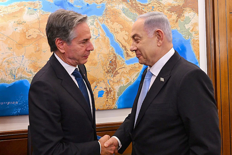 US secretary of state Antony Blinken and Benjamin Netanhayu shake hands in front of a mapof the MIddle East.