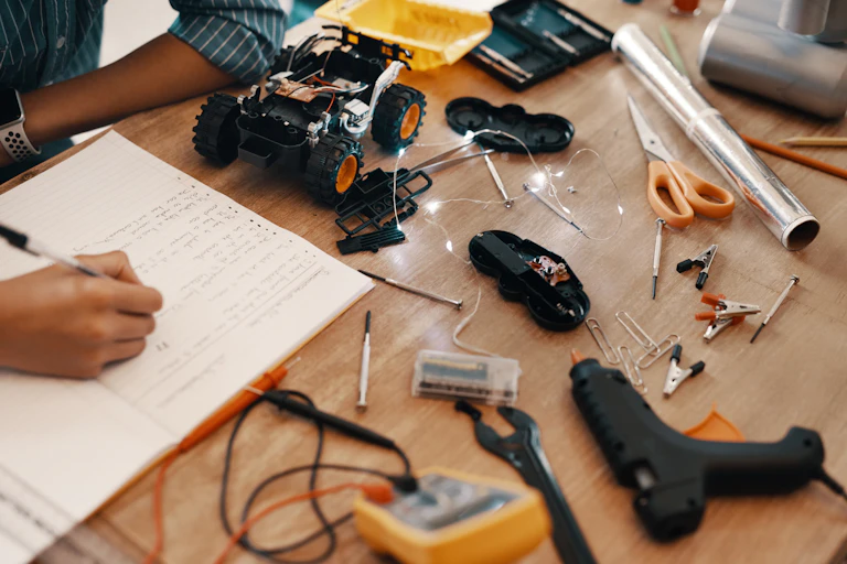 A desk covered in tools and a hand writing in a book