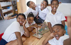 School children laughing and pulling faces around an item they have made from cardboard
