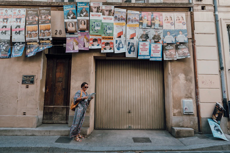 Une femme attend dans une rue d'Avignon avec des affiches de différents spectacles.
