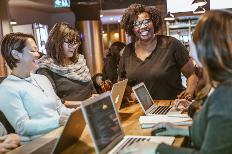 Adults sitting around a table with laptops in discussion.