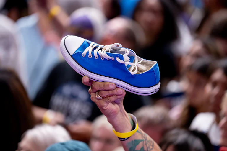 Arm with tattoos and yellow bracelet holds up a blue sneaker.