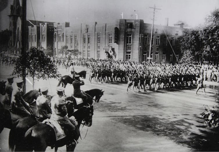 A black and white photo depicts a ;arge formation of soldiers in military dress.