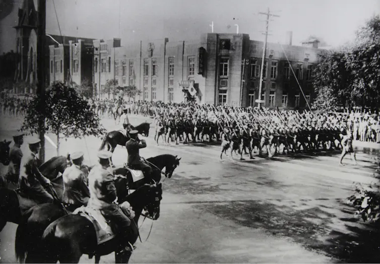 A black and white photo depicts a ;arge formation of soldiers in military dress.