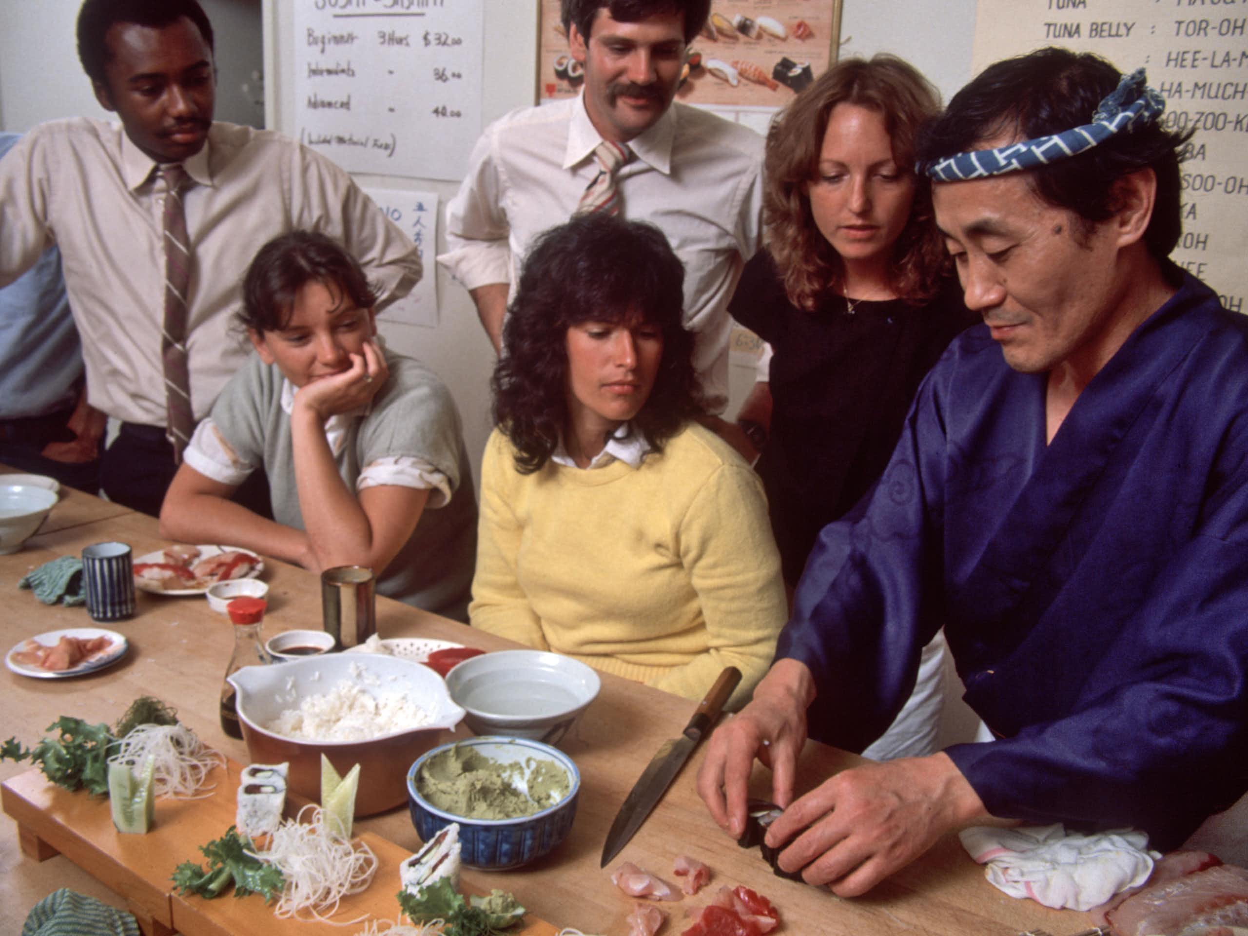 Japanese chef demonstrates something with food as people look on