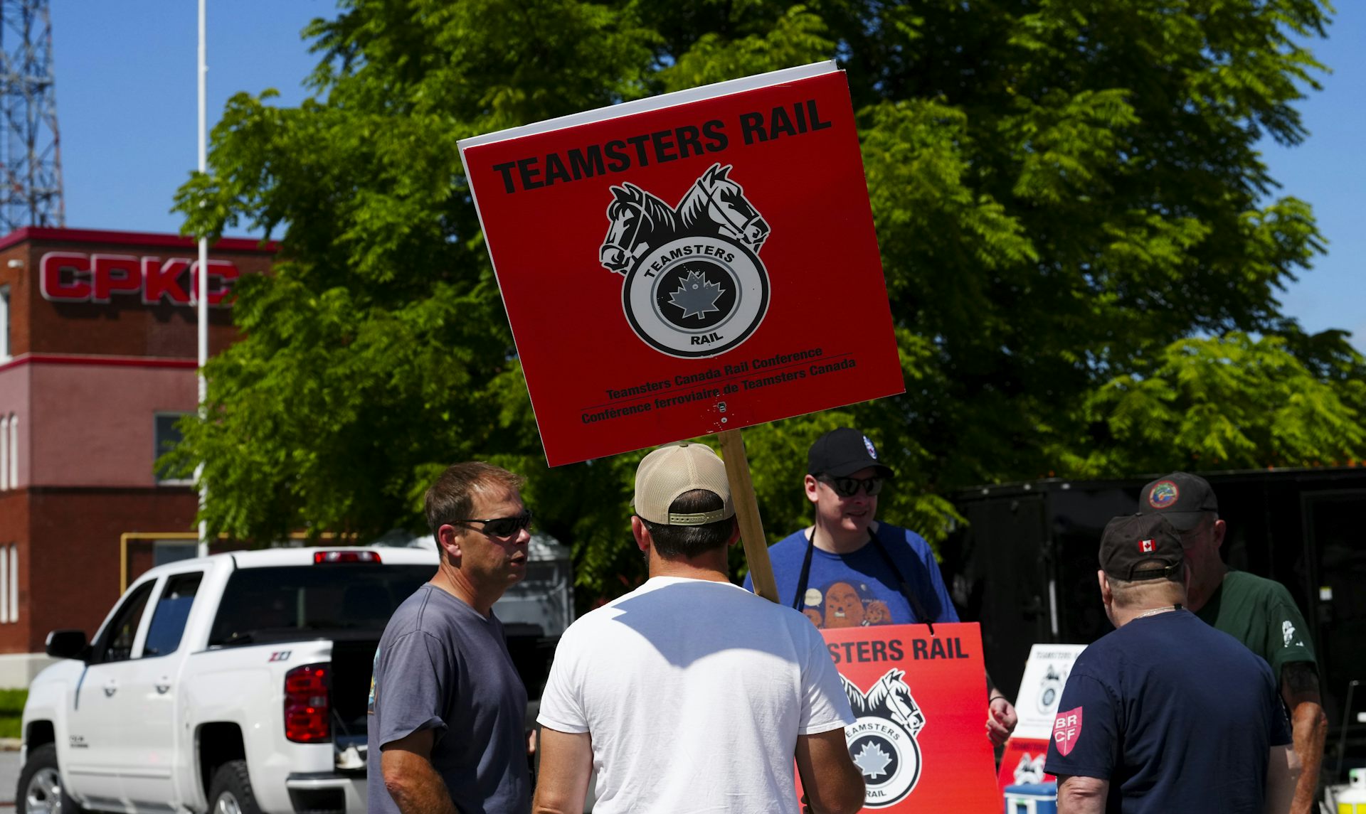 A group of men in t-shirts and baseball caps holding signs that say 'Teamsters Rail'
