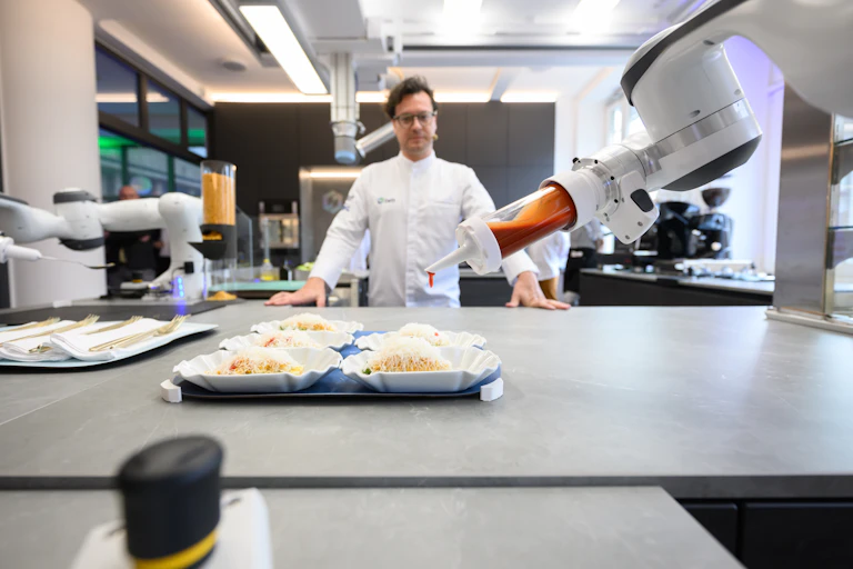 two robotic arms positioned over a table as a man in a white jacket looks on