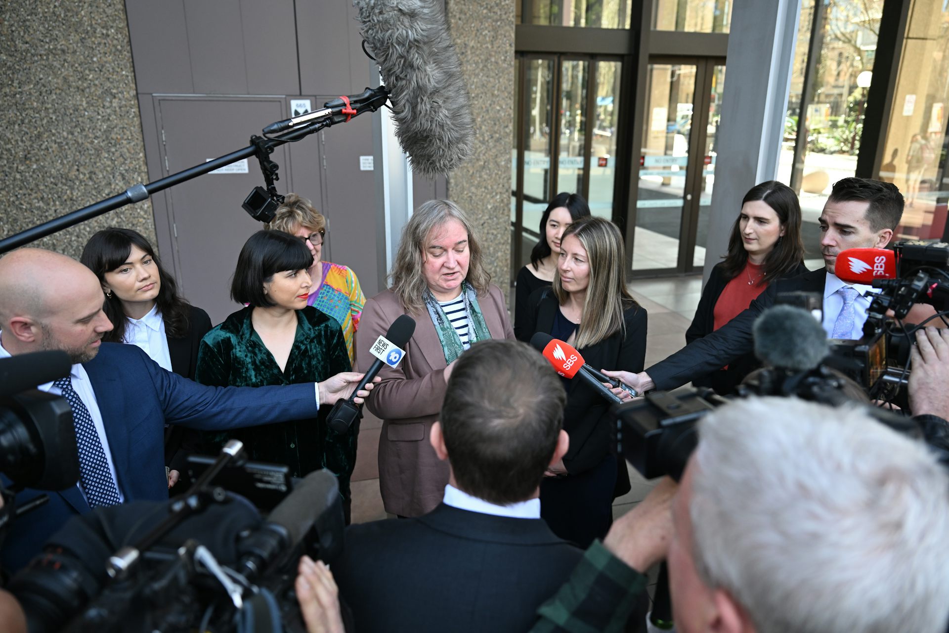 A woman reads from a piece of paper to a large press pack