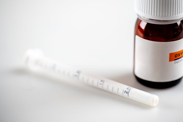 A bottle of oxycodone next to an oral syringe.
