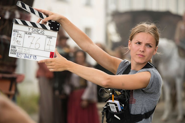 A young woman holding a clapper board on a film set.