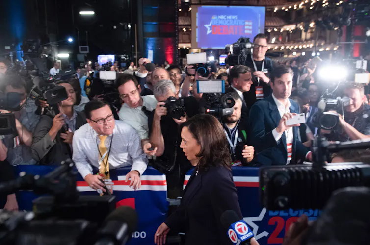 A woman walks past a large group of people holding cameras and microphones.