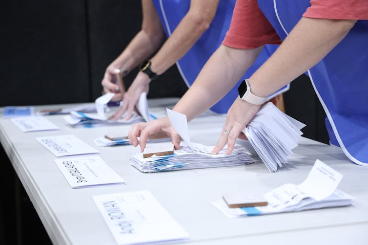 Hands count white ballot papers on a table.