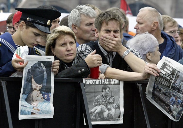 A group of people some obviously in grief hold newspaper front pages depicting injured and dead people.