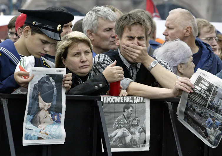 A group of people some obviously in grief hold newspaper front pages depicting injured and dead people.