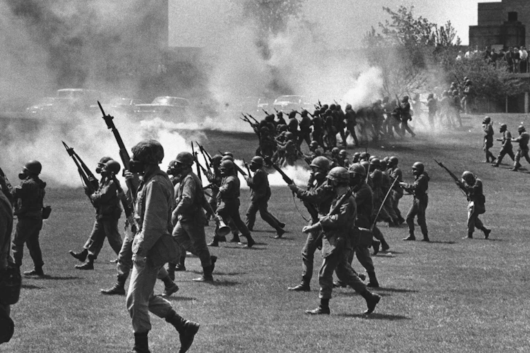 Soldiers carrying guns with bayonets move across a smoky green space