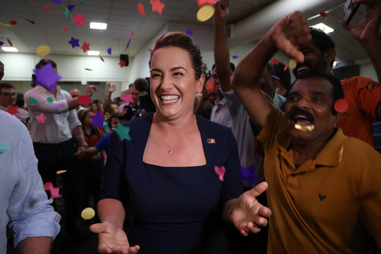 A woman smiles broadly surrounded by confetti and people celebrating
