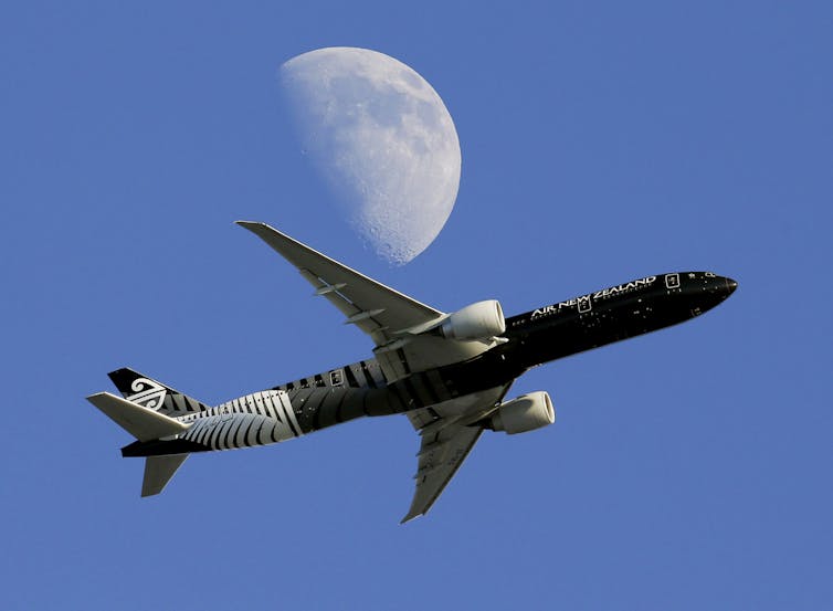plane flying in front of moon in blue sky