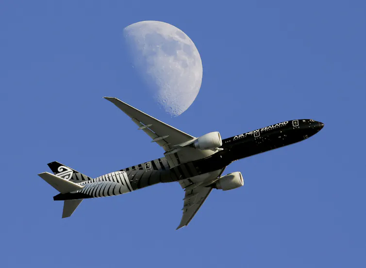 plane flying in front of moon in blue sky