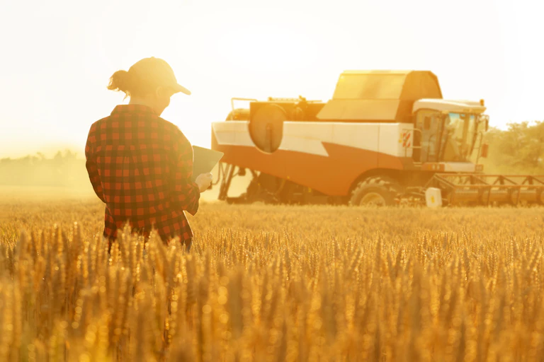 Woman farmer with digital tablet on a background of combine harvester.