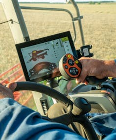 Closeup of hands steering a combine harvester, digital display