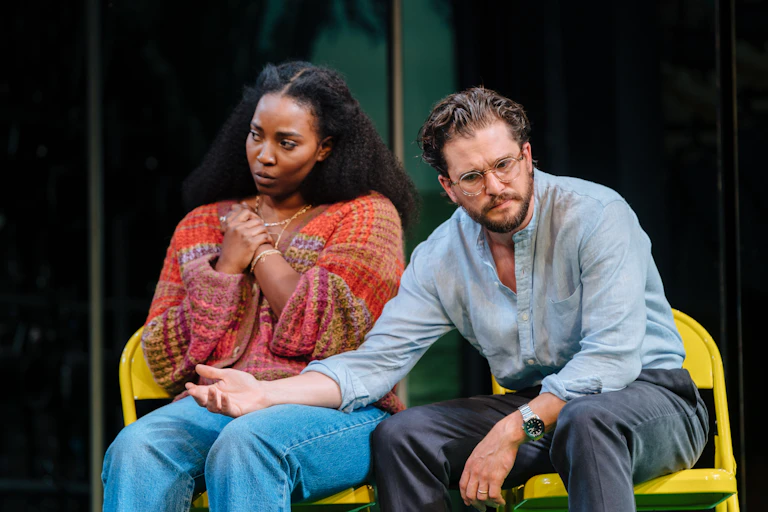 A young black woman and a young white man seated on stage.