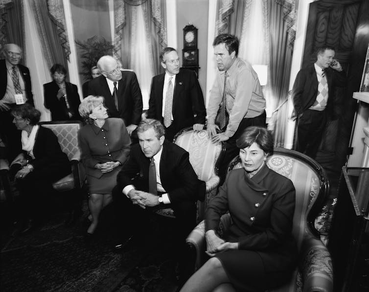 A dozen people in an elegant room watching something on a television.
