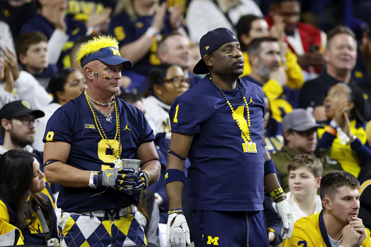 Two men wearing blue and gold among a big stadium crowd.