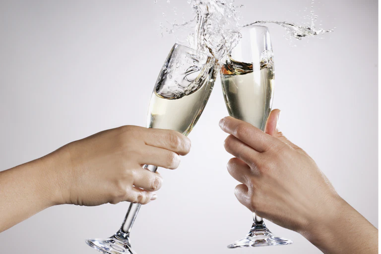 Two hands clinking overflowing champagne flutes