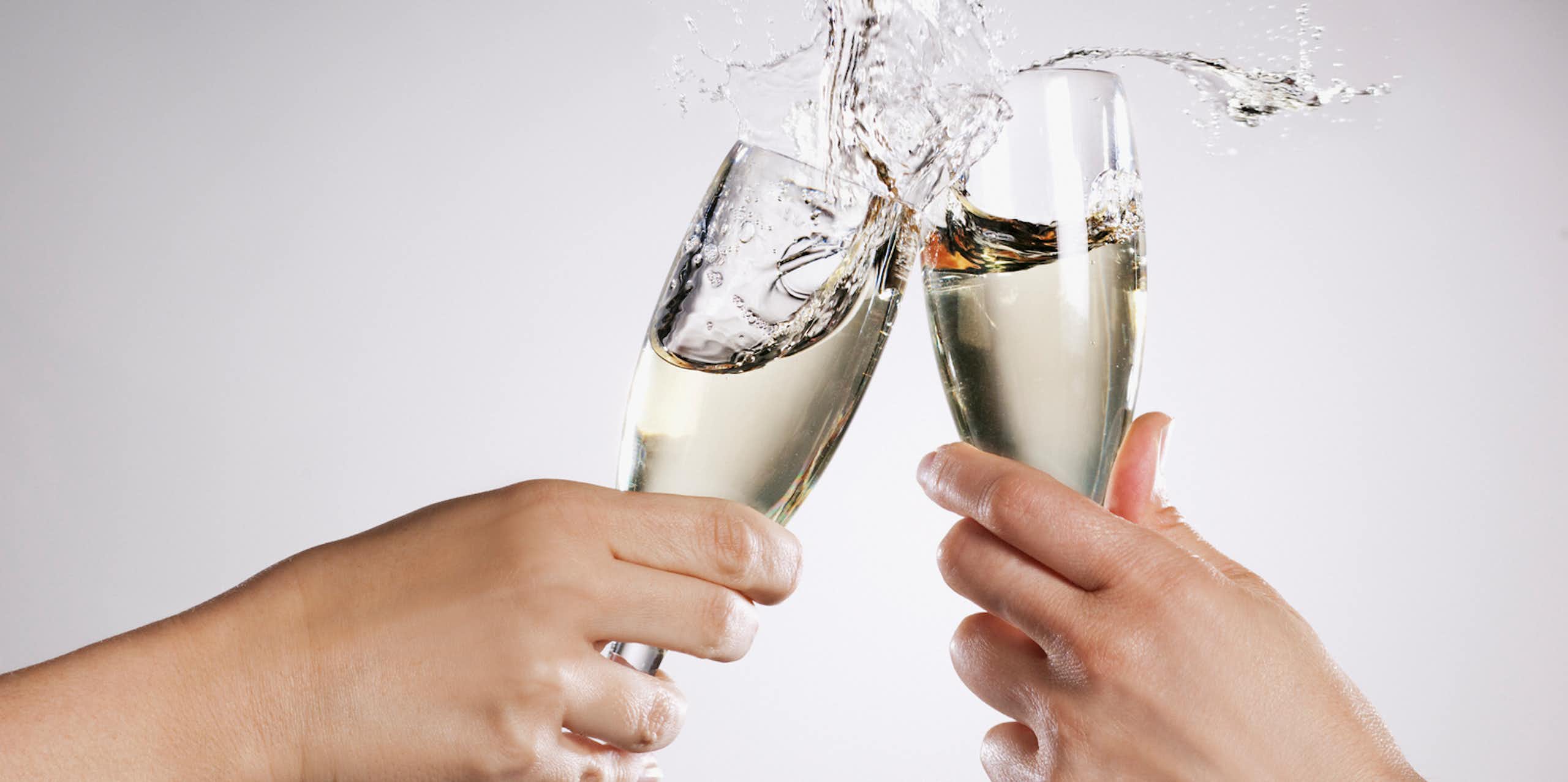 Two hands clinking overflowing champagne flutes