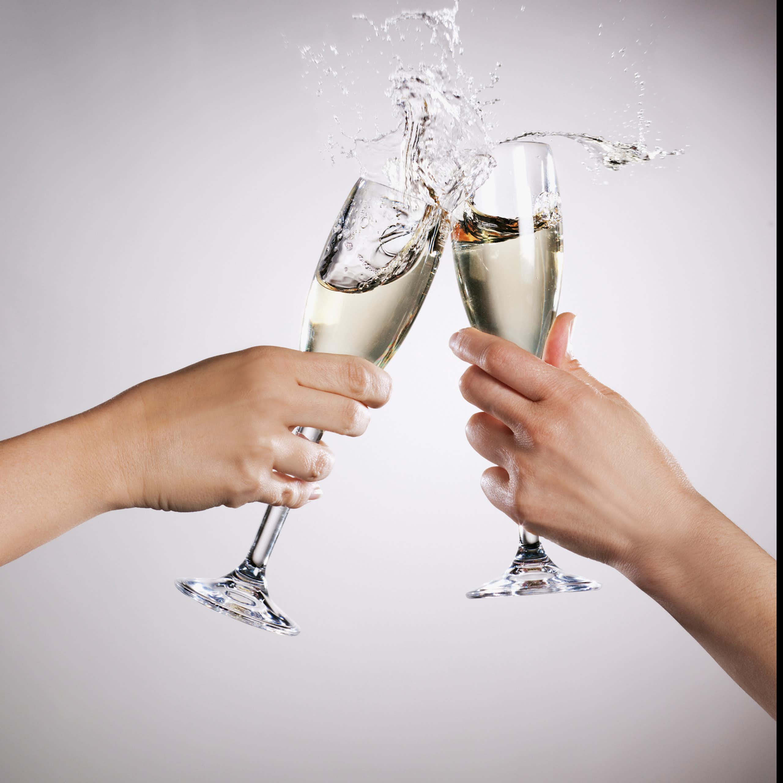 Two hands clinking overflowing champagne flutes