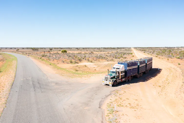 A big truck drives from an unsealed road onto a different rural road.