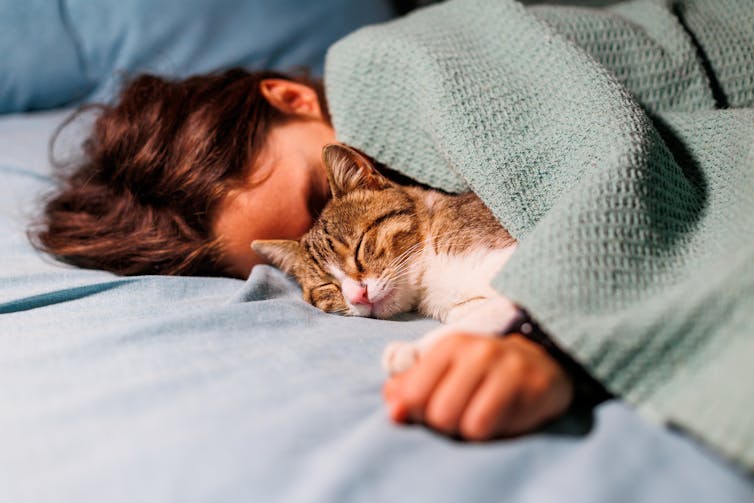 A young man sleeps next to a sleeping cat.