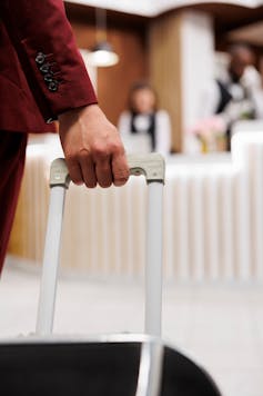 person holding baggage enters hotel reception front desk
