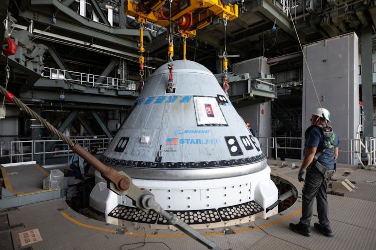 A cone shaped white capsule with a worker standing next to it in a hangar.