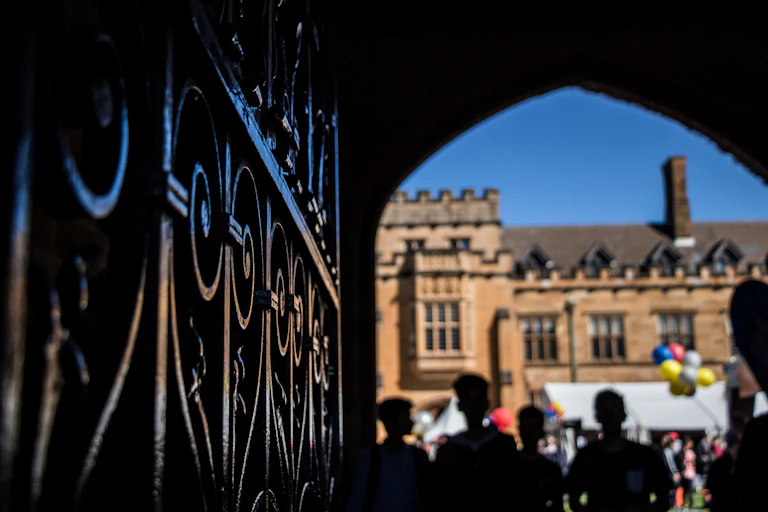 An iron gate in front of a sandstone building. The online of five young people is shown in shadow.
