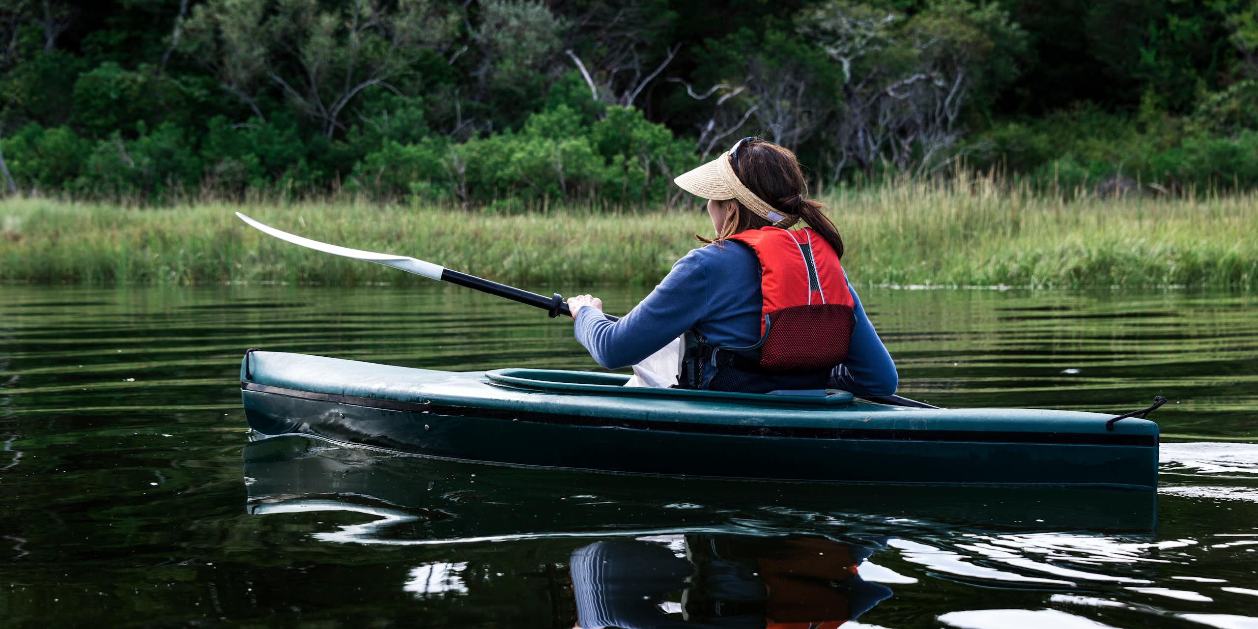 A woman paddles a kayak on a quiet river