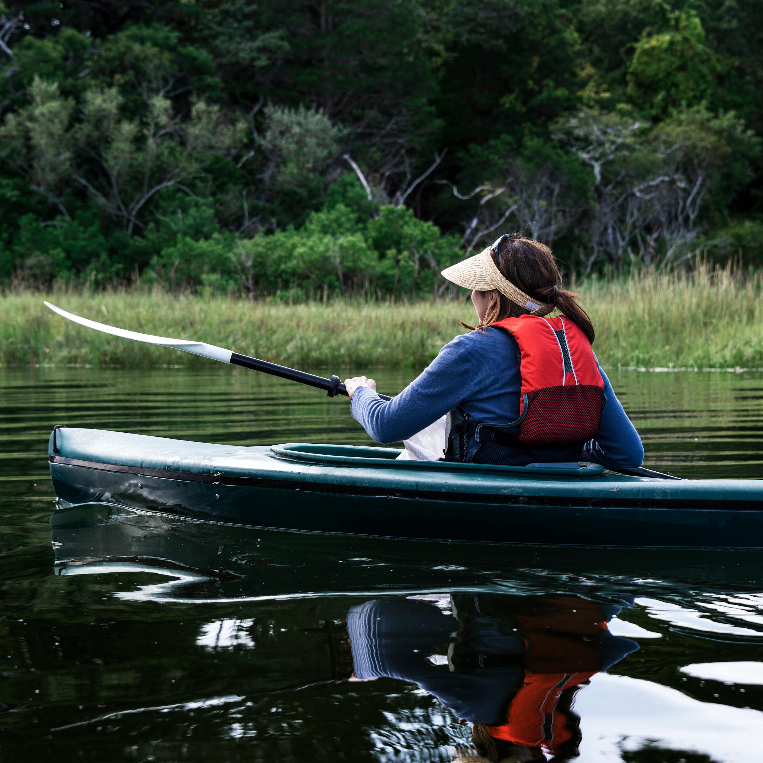 A woman paddles a kayak on a quiet river