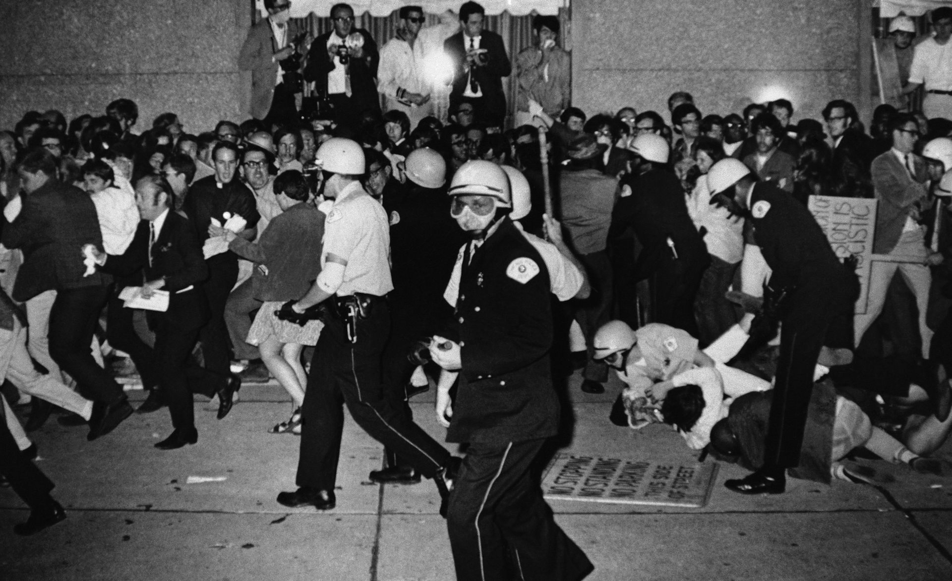 A black and white photo shows armed police officers fighting with protesters.