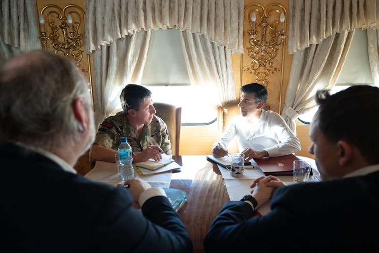 Gwyn Jenkins e Rishi Sunak sentados um ao lado do outro conversando em um trem ricamente decorado.