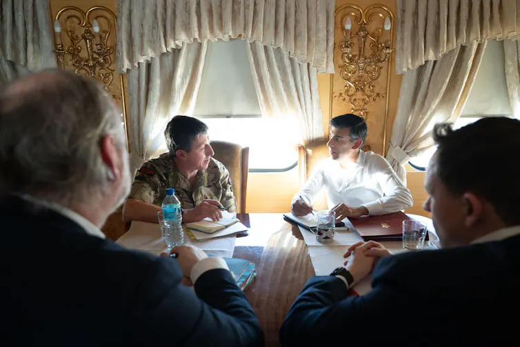 Gwyn Jenkins and Rishi Sunak sitting next to each other and talking on an ornately decorated train.
